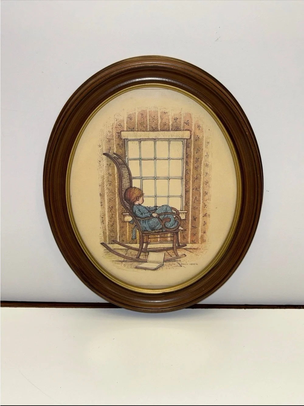 Vintage oval framed wall art piece featuring a girl in a rocking chair by a wind